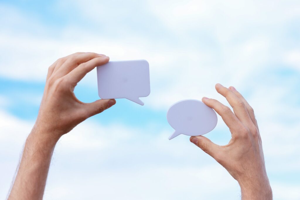 Two hands holding blank speech bubbles against a blue sky, illustrating communication and marketing messaging