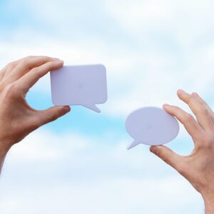Two hands holding blank speech bubbles against a blue sky, illustrating communication and marketing messaging